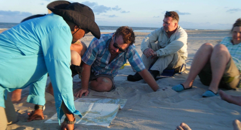 a group of veterans sit on the beach looking at a map